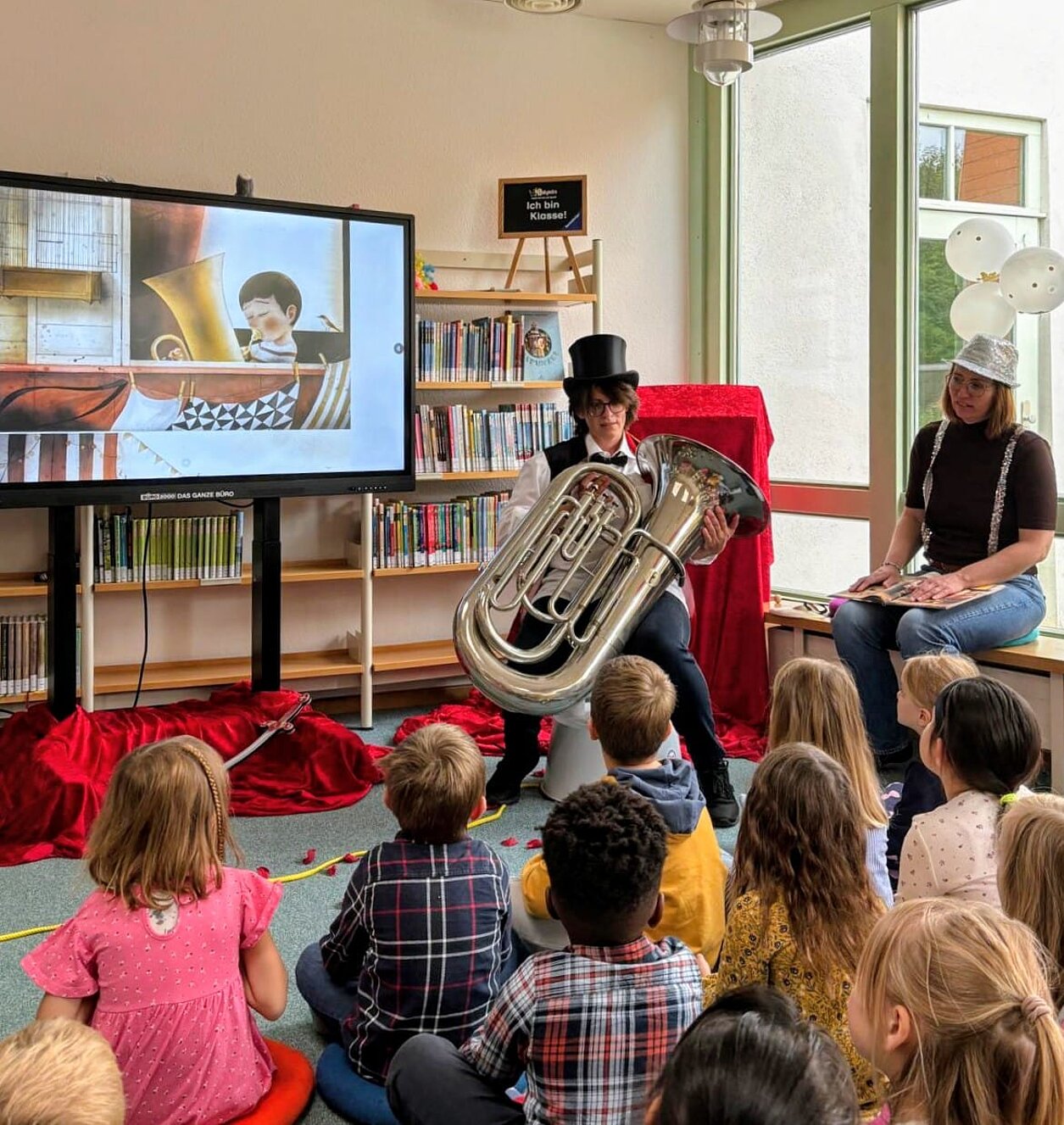 Imposant: Viola Donner und Christina Sürig zeigen den Kindern Adams „echte“ Tuba! Zirkuswoche_zum_Weltkindertag_Adam_und_seine_Tuba_Stadtbuecherei_Bild_1_Tuba